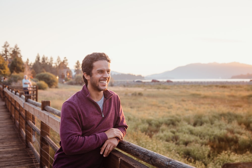 man in purple hoodie sitting on brown wooden fence during daytime