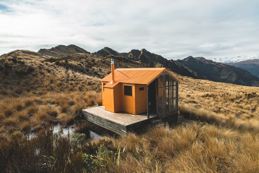 brown wooden house on green grass field near mountain during daytime