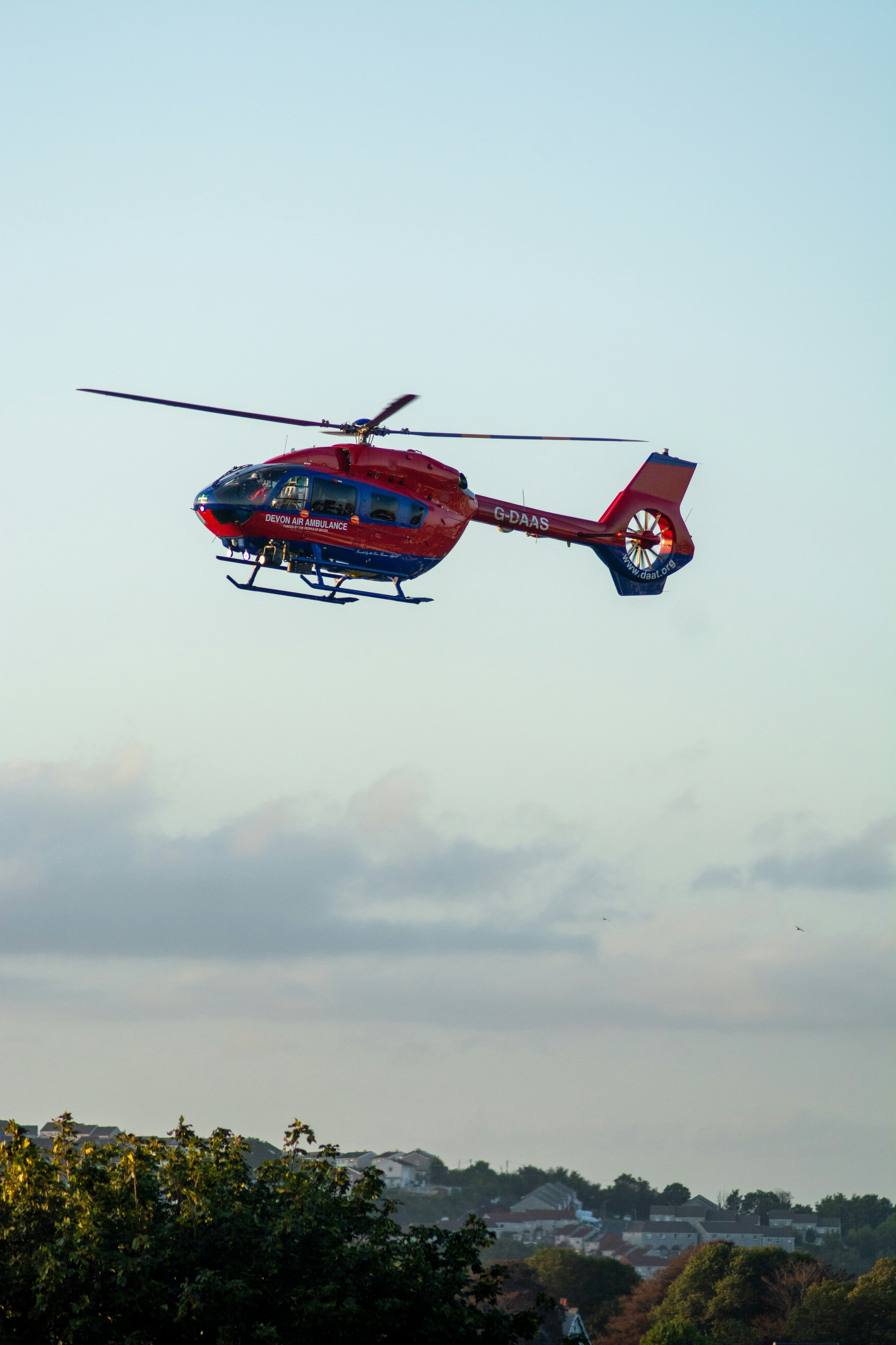 red helicopter flying under white clouds during daytime