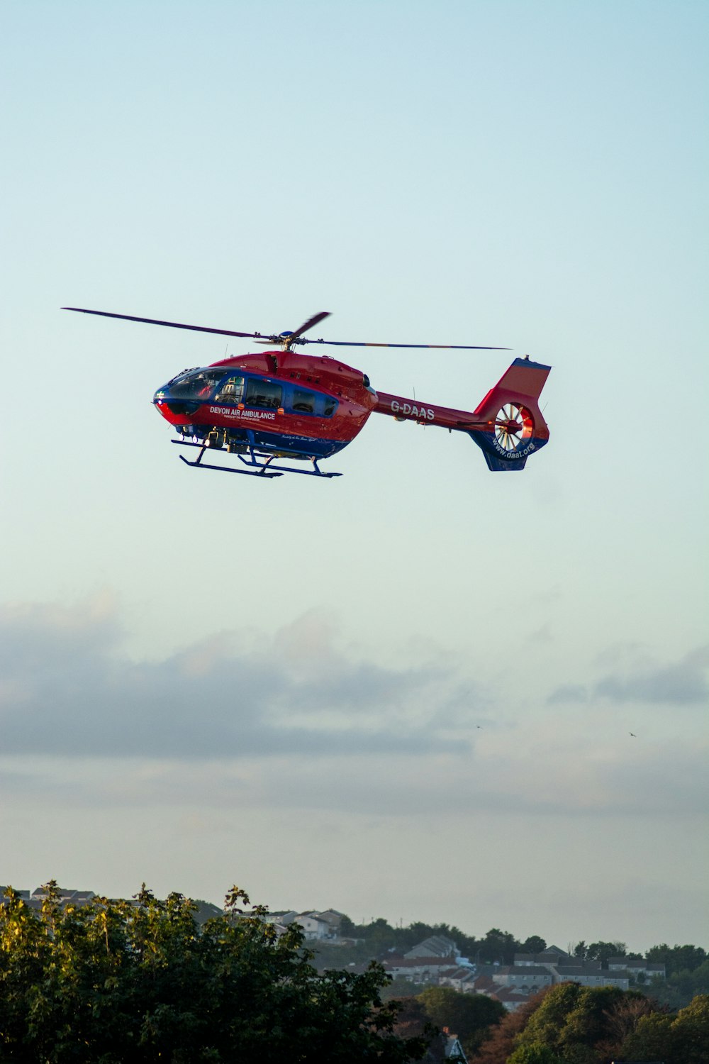 red helicopter flying under white clouds during daytime