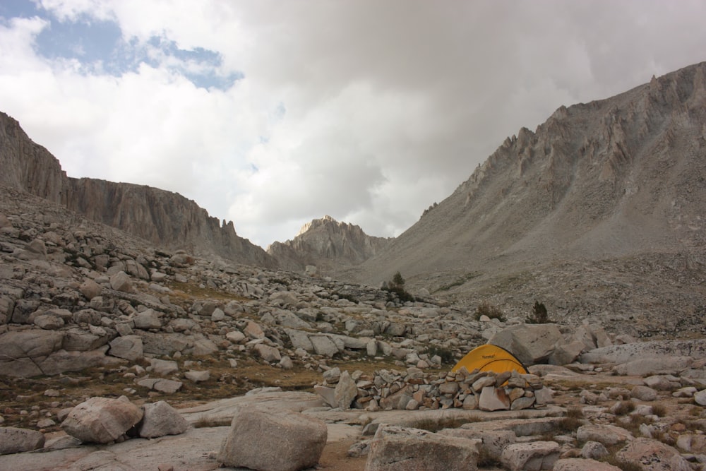 yellow dome tent on rocky ground near mountains under white cloudy sky during daytime