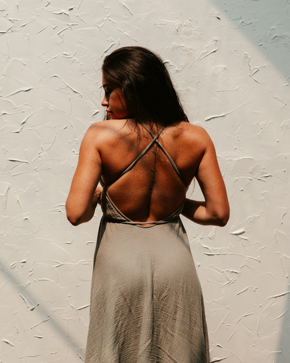 woman in gray spaghetti strap dress standing beside white wall