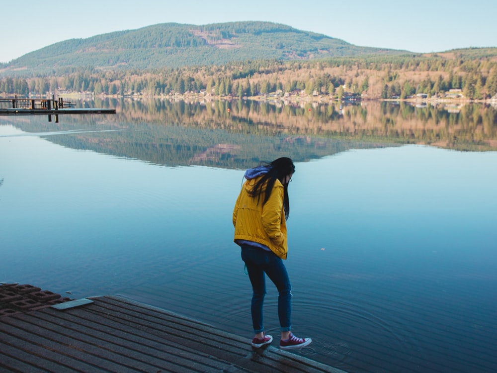 man in yellow jacket and black pants standing on dock during daytime