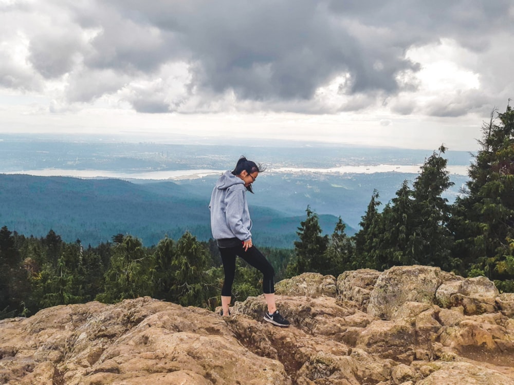 man in blue dress shirt and black pants standing on brown rock formation near green trees