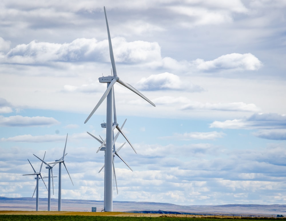 white wind turbines on green grass field under white clouds and blue sky during daytime