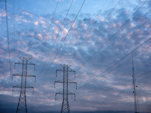 Two transmission towers and a radio antenna rise against a backdrop of an evening or early morning sky, filled with soft, scattered clouds. The sky transitions from light to darker shades of blue, creating a tranquil scene.