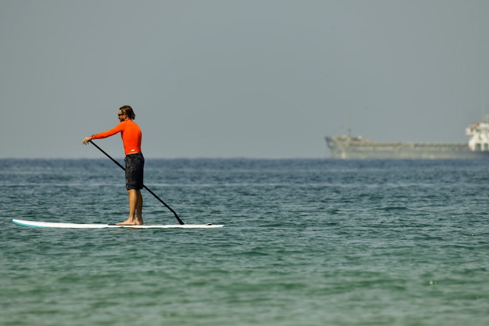 man in orange shirt and black shorts riding on white surfboard during daytime
