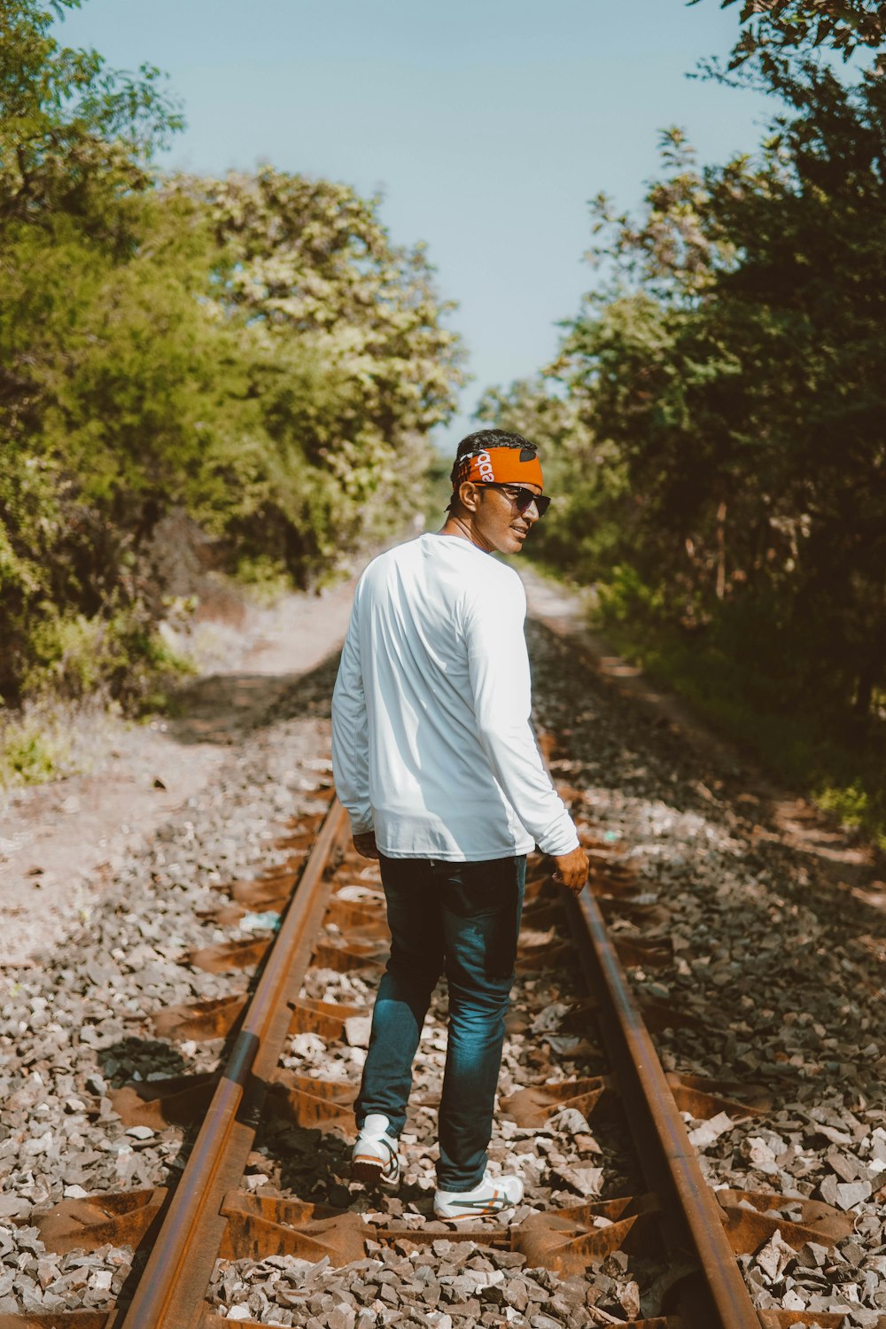 man in white long sleeve shirt and black pants standing on train rail during daytime