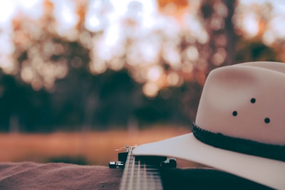 Close-up of a musician playing an acoustic guitar with a cowboy hat nearby.