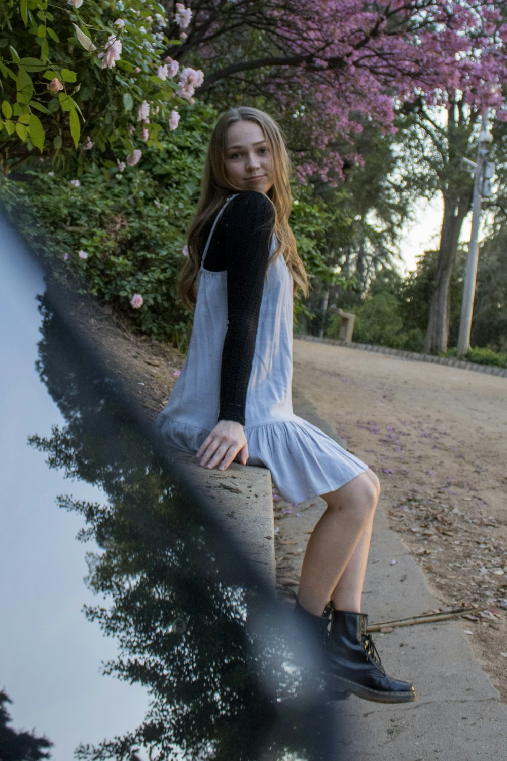 woman in black long sleeve shirt and white skirt sitting on gray concrete pathway during daytime