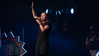 Elegant female Brazilian singer performing on stage with soft colorful lights in background.