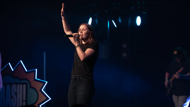 Elegant female Brazilian singer performing on stage with soft colorful lights in background.