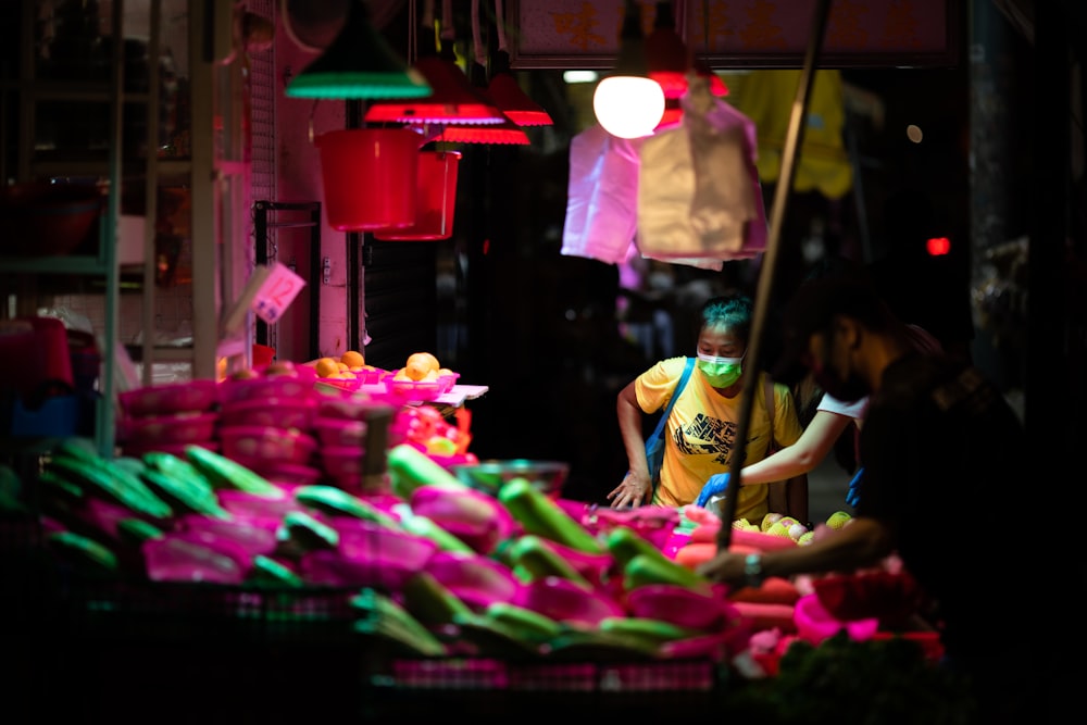 woman in white tank top standing in front of vegetable stand