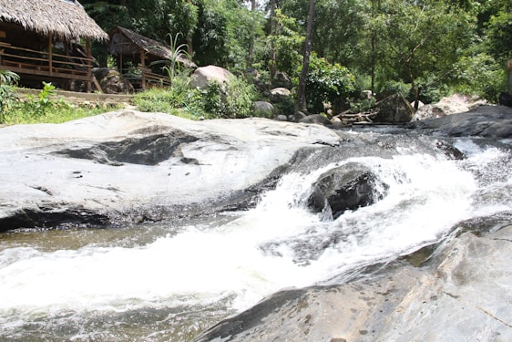 A serene view of the Hennops River flowing through the guest house grounds with traditional Zulu huts and colorful decorations.