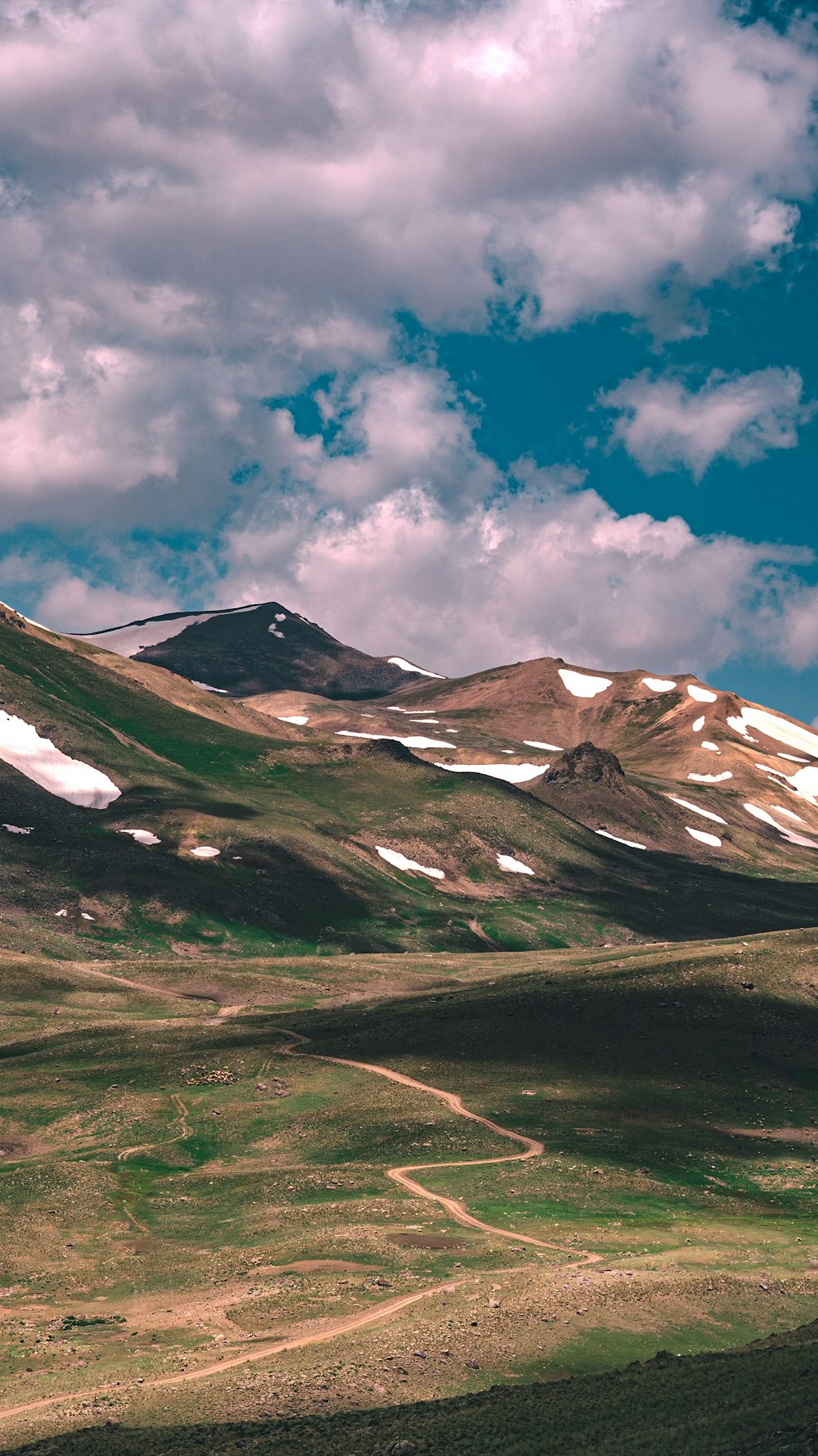 green grass field near mountain under blue sky during daytime