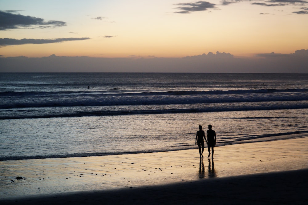 silhouette of 2 people walking on beach during sunset