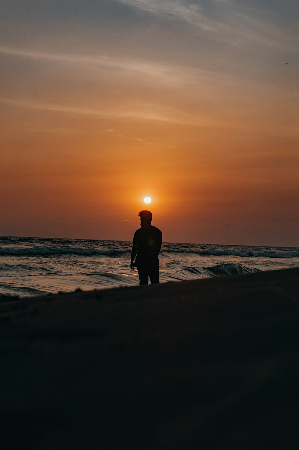 silhouette of man and woman standing on beach during sunset