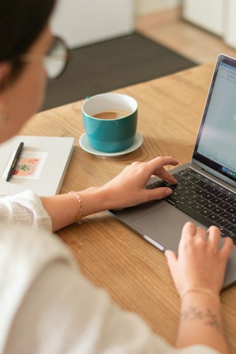 Close-up of a hand writing follow-up notes in a planner next to a laptop