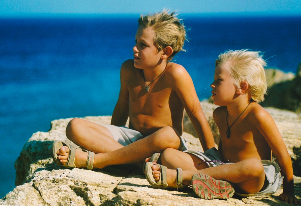 woman in brown bikini sitting beside topless boy on beach during daytime