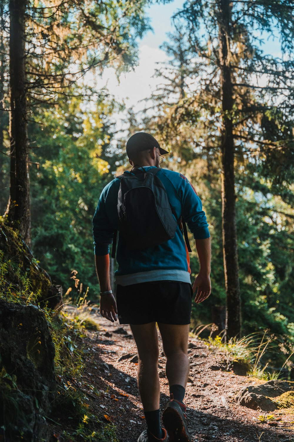 man in blue and black shirt and black shorts standing on brown rock in forest during