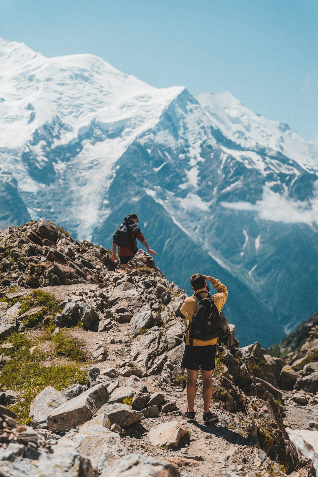 man in yellow shirt and black shorts standing on rocky mountain during daytime