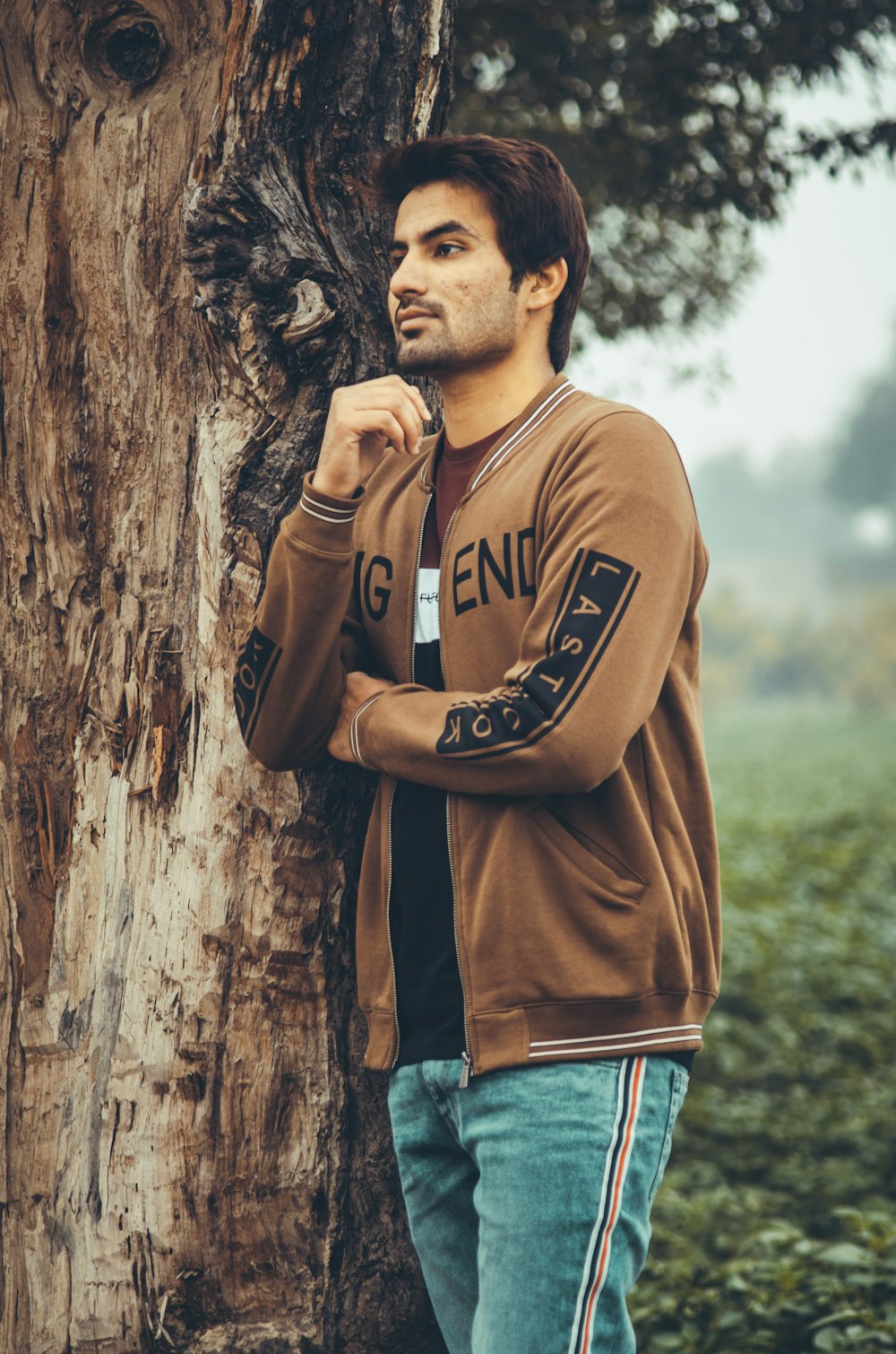 man in brown crew neck t-shirt leaning on brown tree trunk during daytime