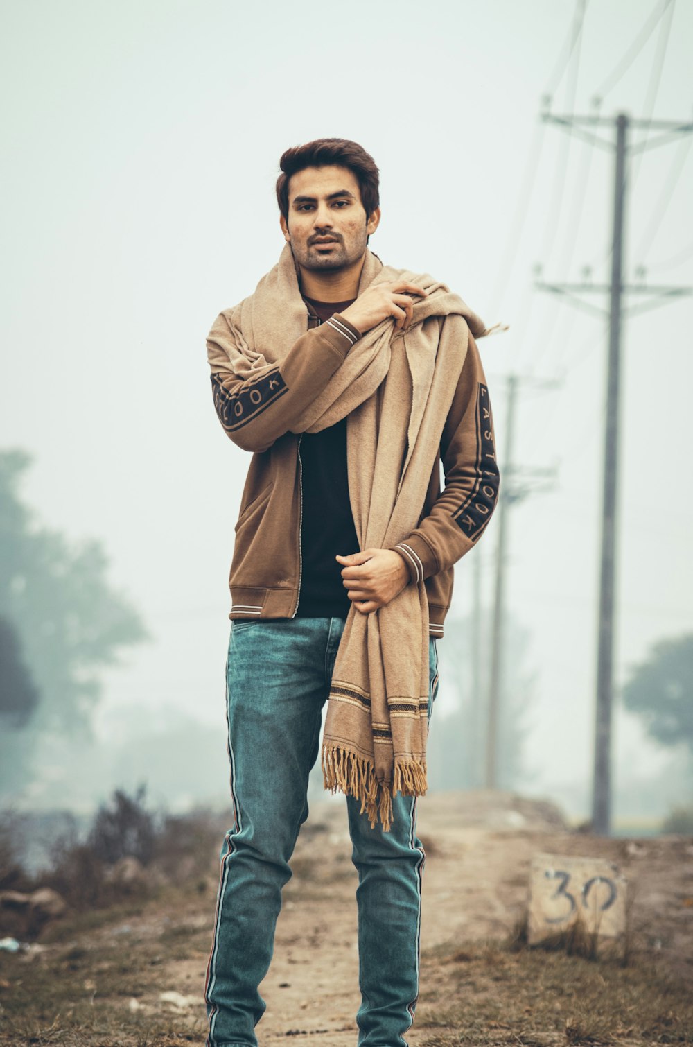 man in brown leather jacket and blue denim jeans standing beside brown tree  trunk during daytime photo – Free Pakistan Image on Unsplash