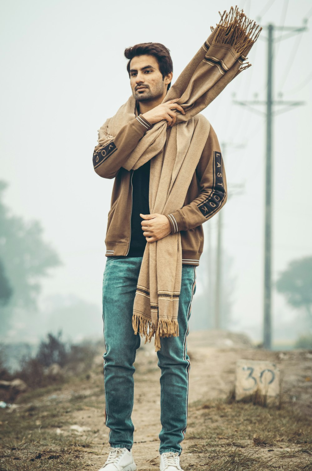 man in brown coat and blue denim jeans standing on brown field