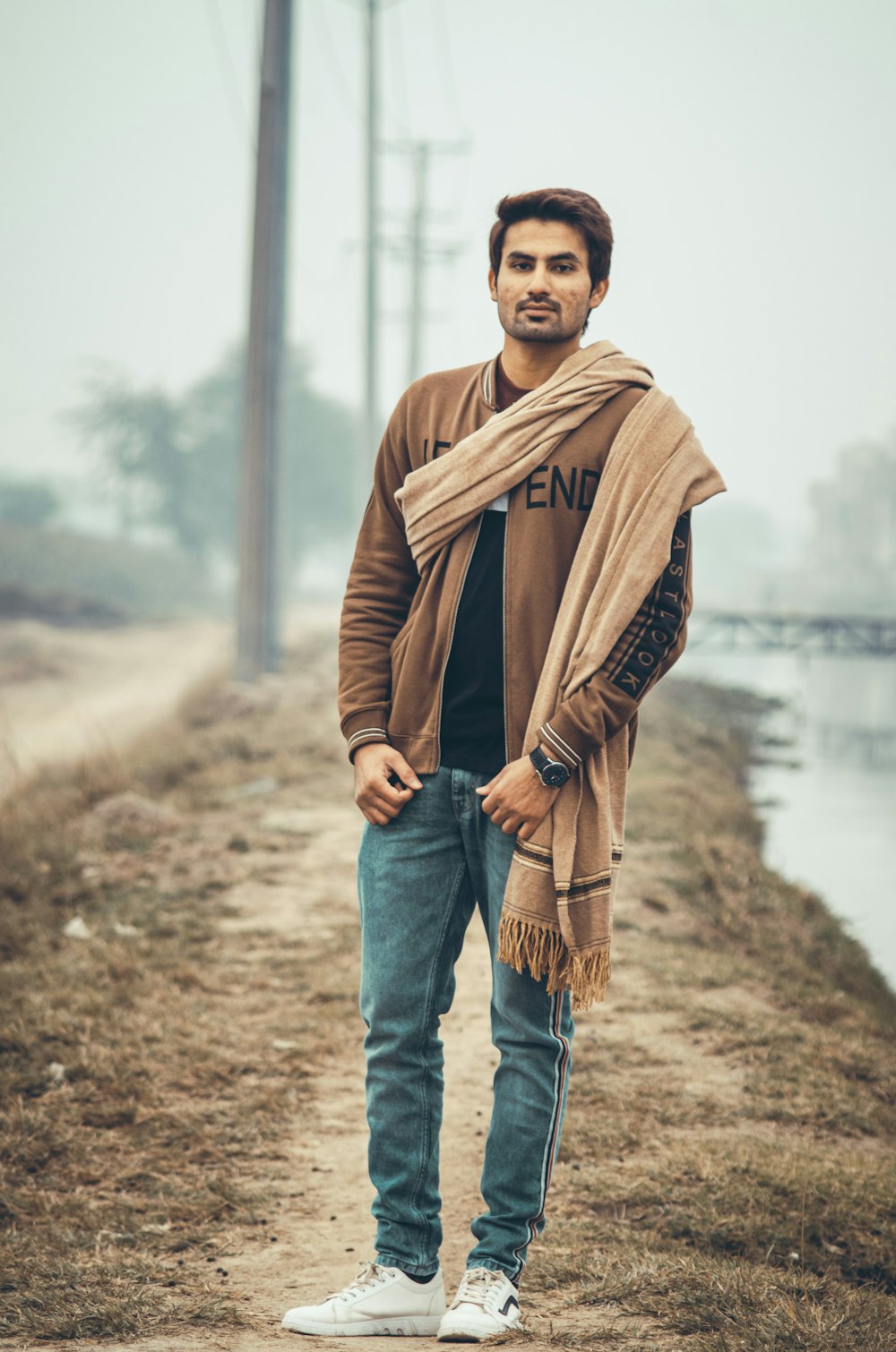 man in brown leather jacket and blue denim jeans standing on brown field during daytime