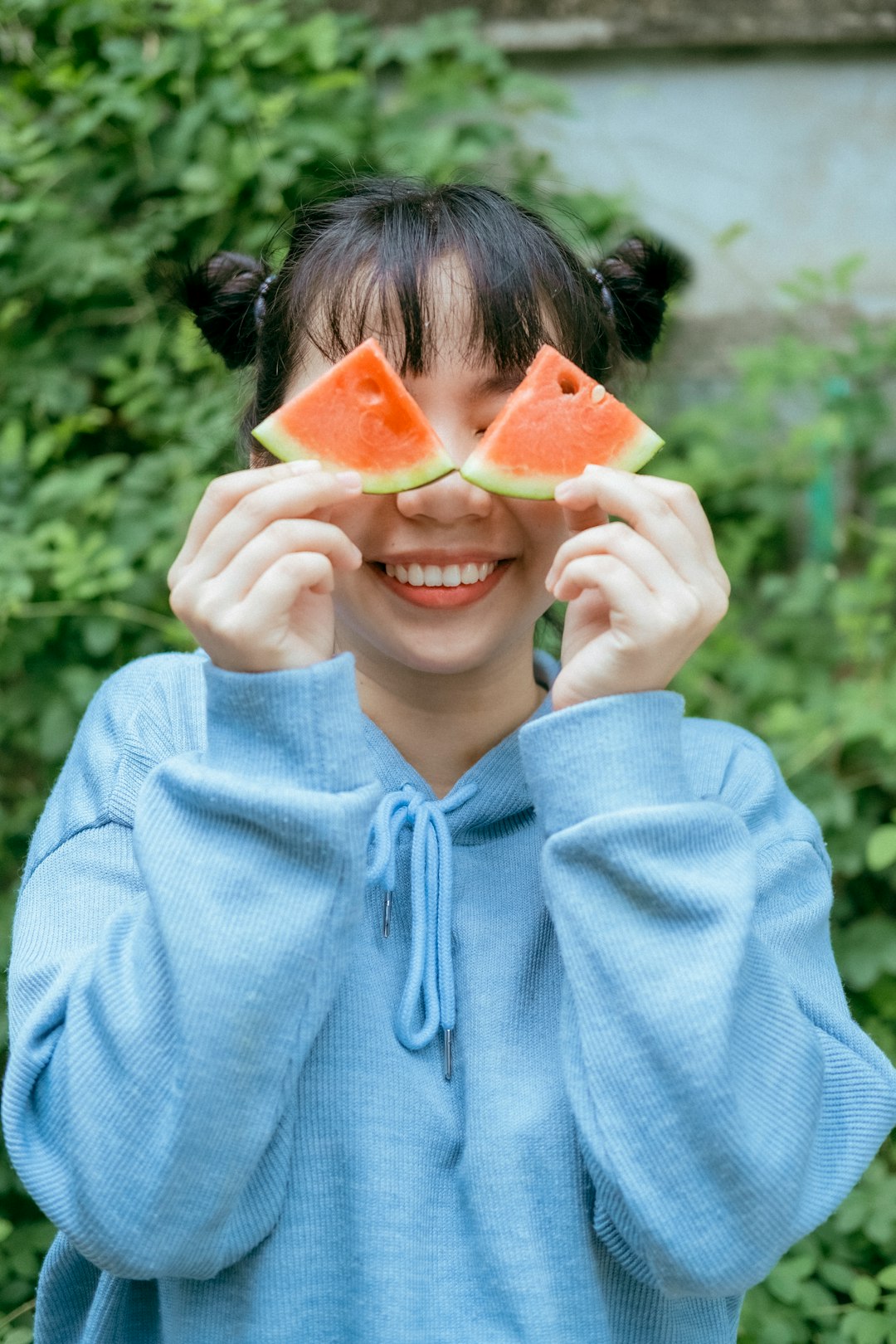 woman in blue hoodie holding sliced watermelon