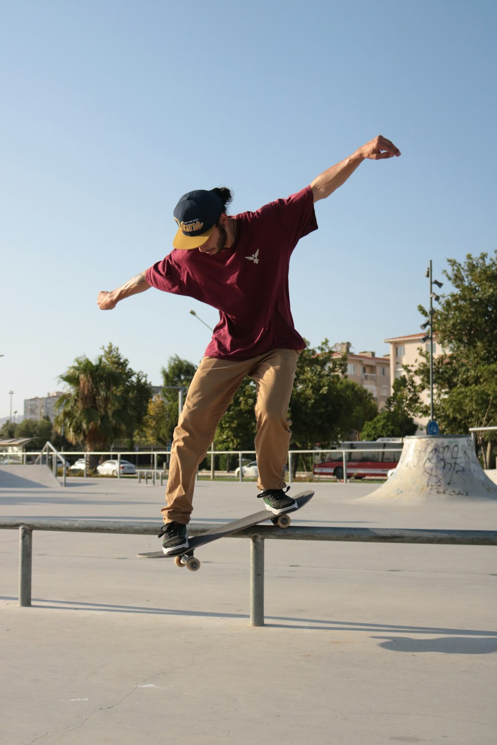 man in red t-shirt and brown pants doing skateboard stunts during daytime