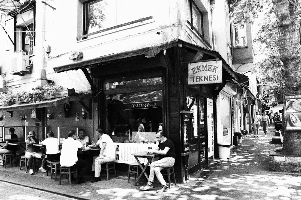 grayscale photo of people sitting on chairs near store