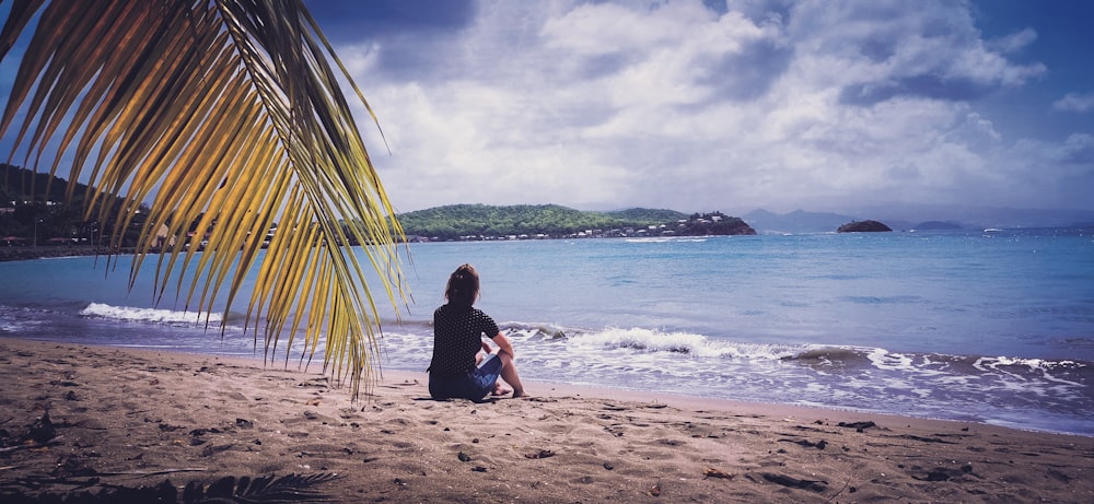 woman in black shirt sitting on beach during daytime