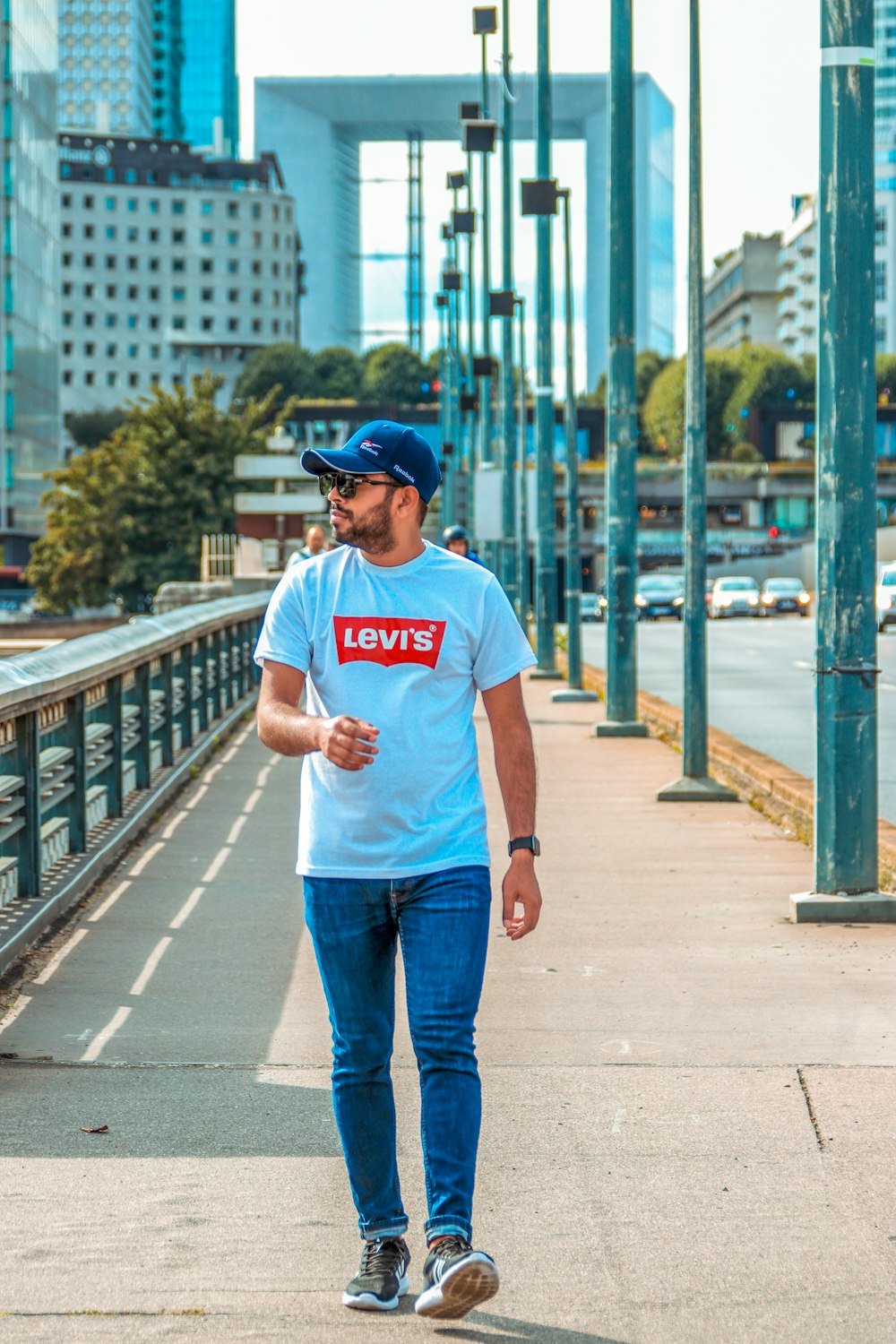 Uomo in t-shirt girocollo bianca e jeans blu in denim in piedi sul ponte durante il giorno