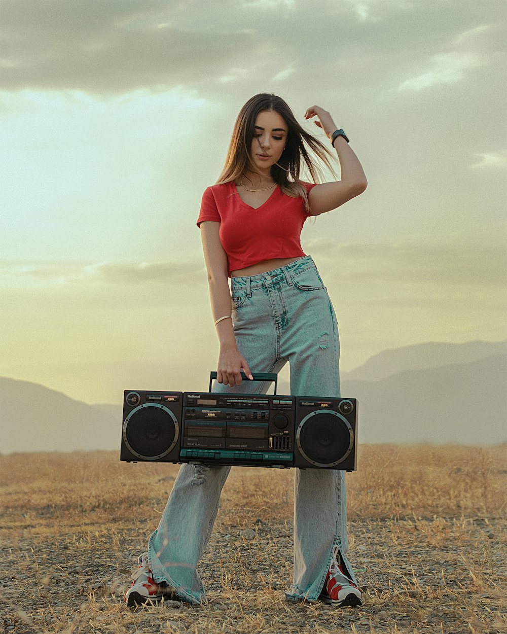 woman in red shirt and blue denim jeans holding black speaker