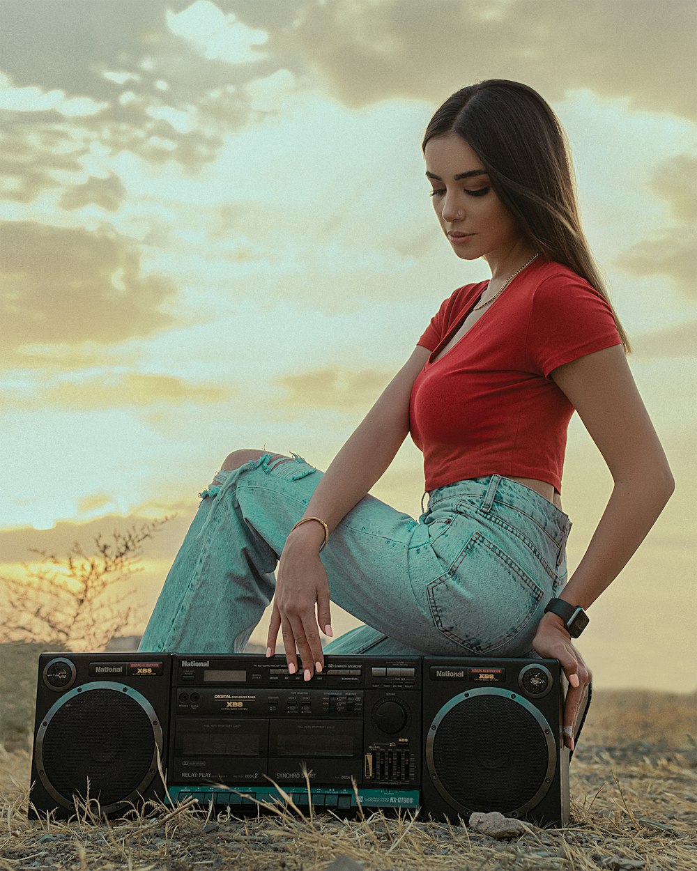 woman in red shirt and blue denim shorts sitting on black sony radio