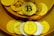 A collection of physical coins representing various cryptocurrencies is arranged on a golden surface. The coins prominently display logos like Bitcoin and Dogecoin, with a mix of gold and silver colors.
