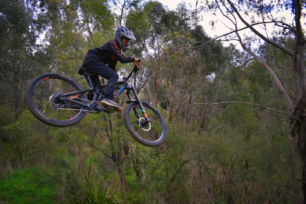 man in black jacket riding black mountain bike on forest during daytime