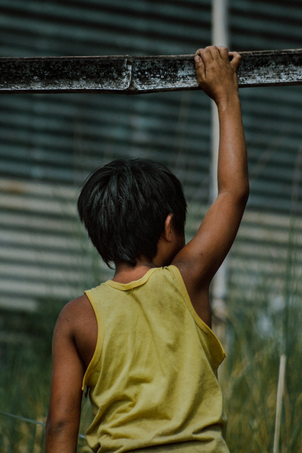 boy in yellow tank top holding on black metal bar during daytime