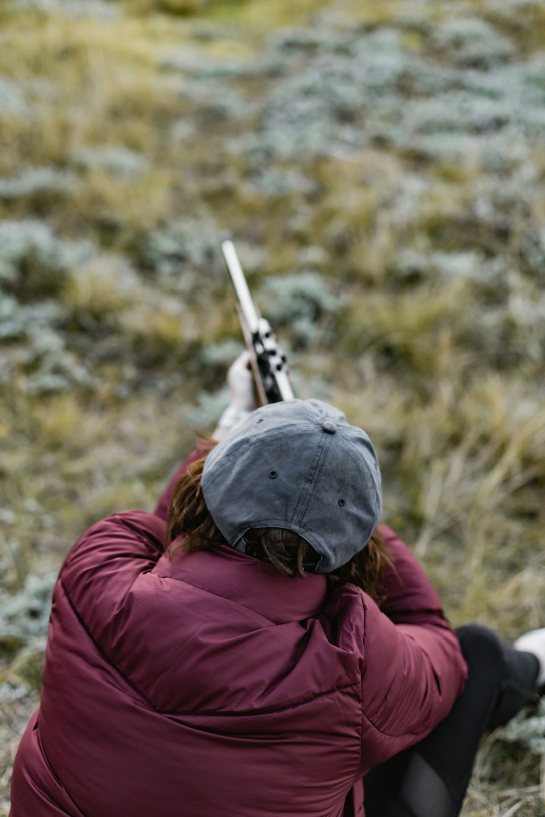 person in red jacket wearing black cap holding rifle