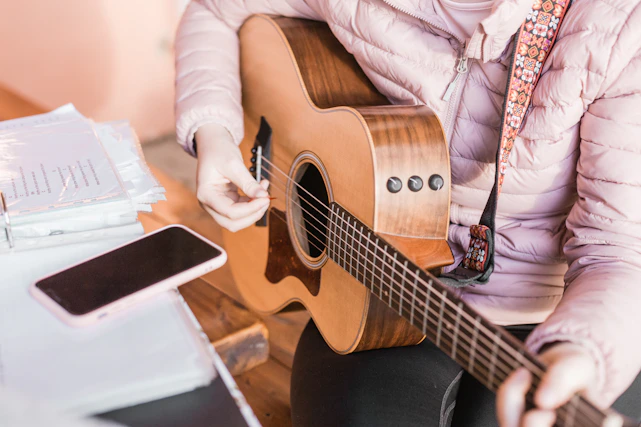 person in pink jacket playing brown acoustic guitar