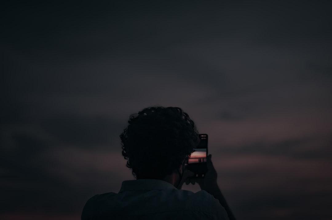 man taking photo using black dslr camera, Photo of a photographer capturing the beauty of beach and sunset.