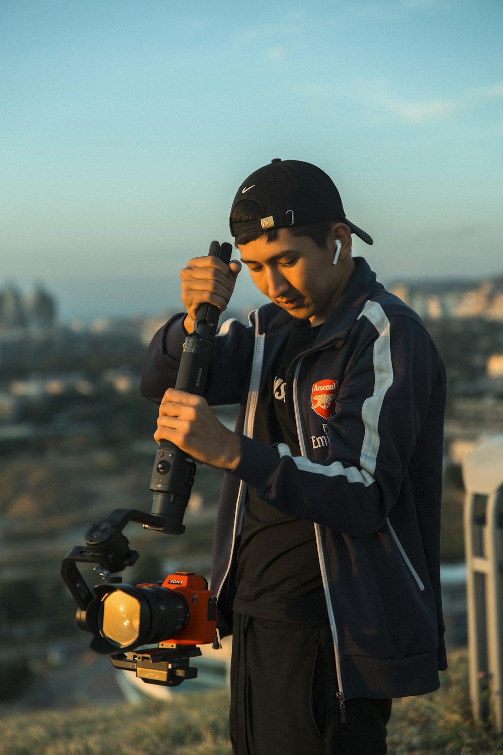 man in black and orange jacket holding black and orange dslr camera