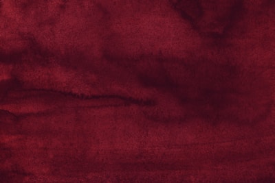 A textured background featuring varying shades of deep red with hints of maroon. The surface appears to have an uneven, watercolor-like wash that creates a sense of depth and movement.