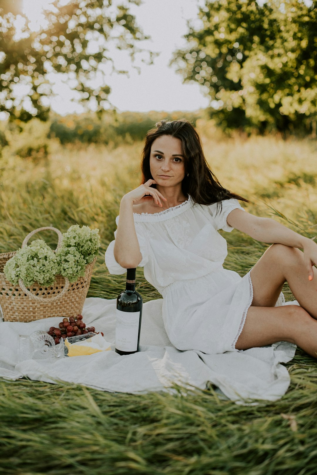 woman in white dress sitting on table with wine glass and wine glass