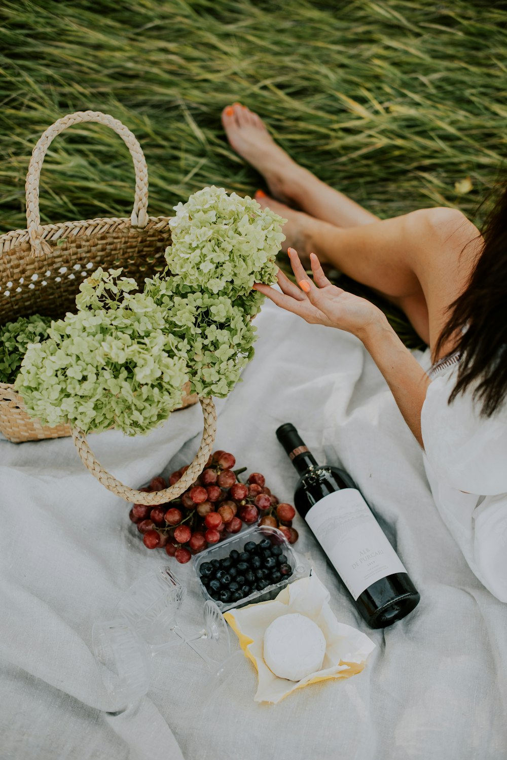 woman in white dress holding brown woven basket with white and black bottles