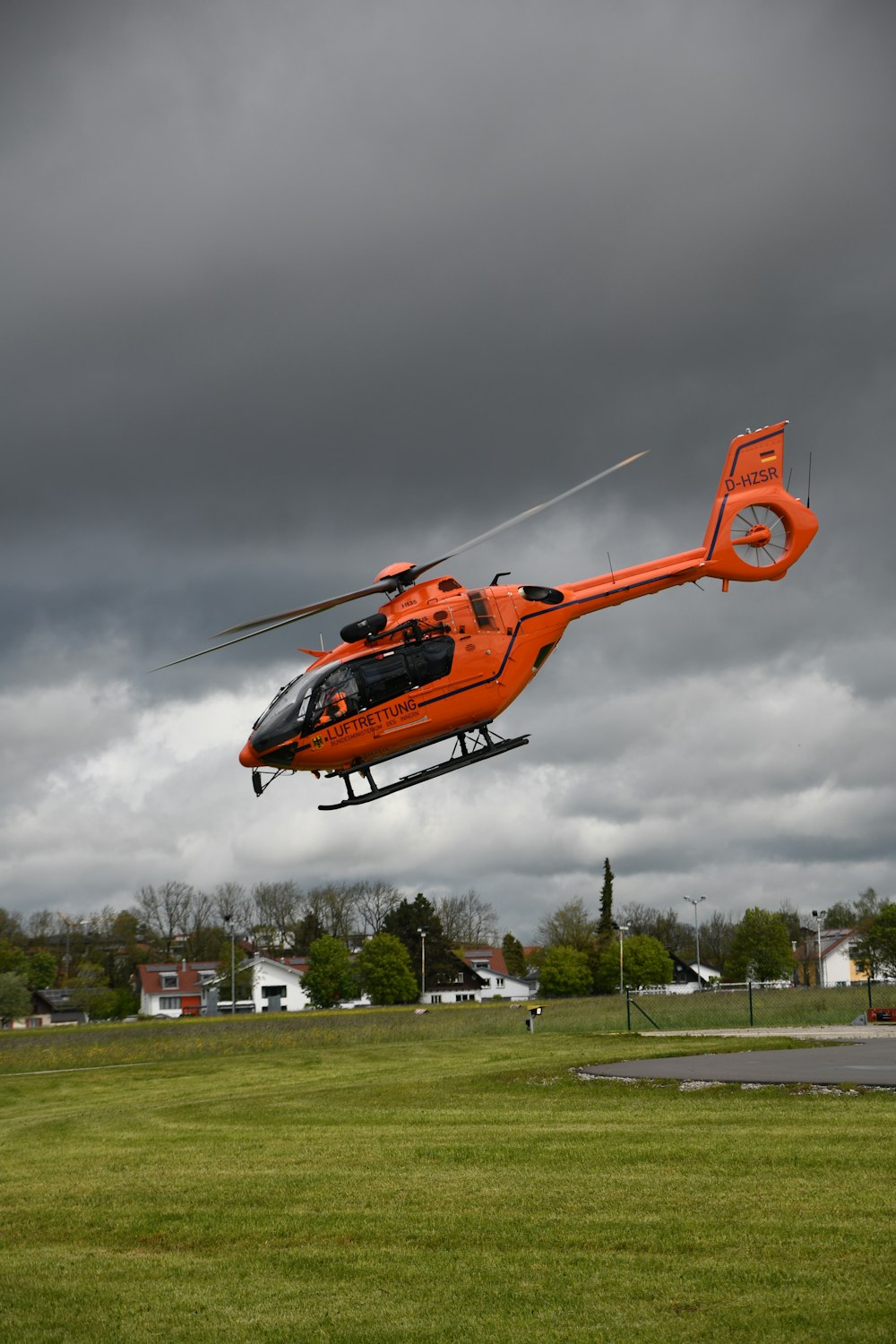an orange helicopter flying through a cloudy sky