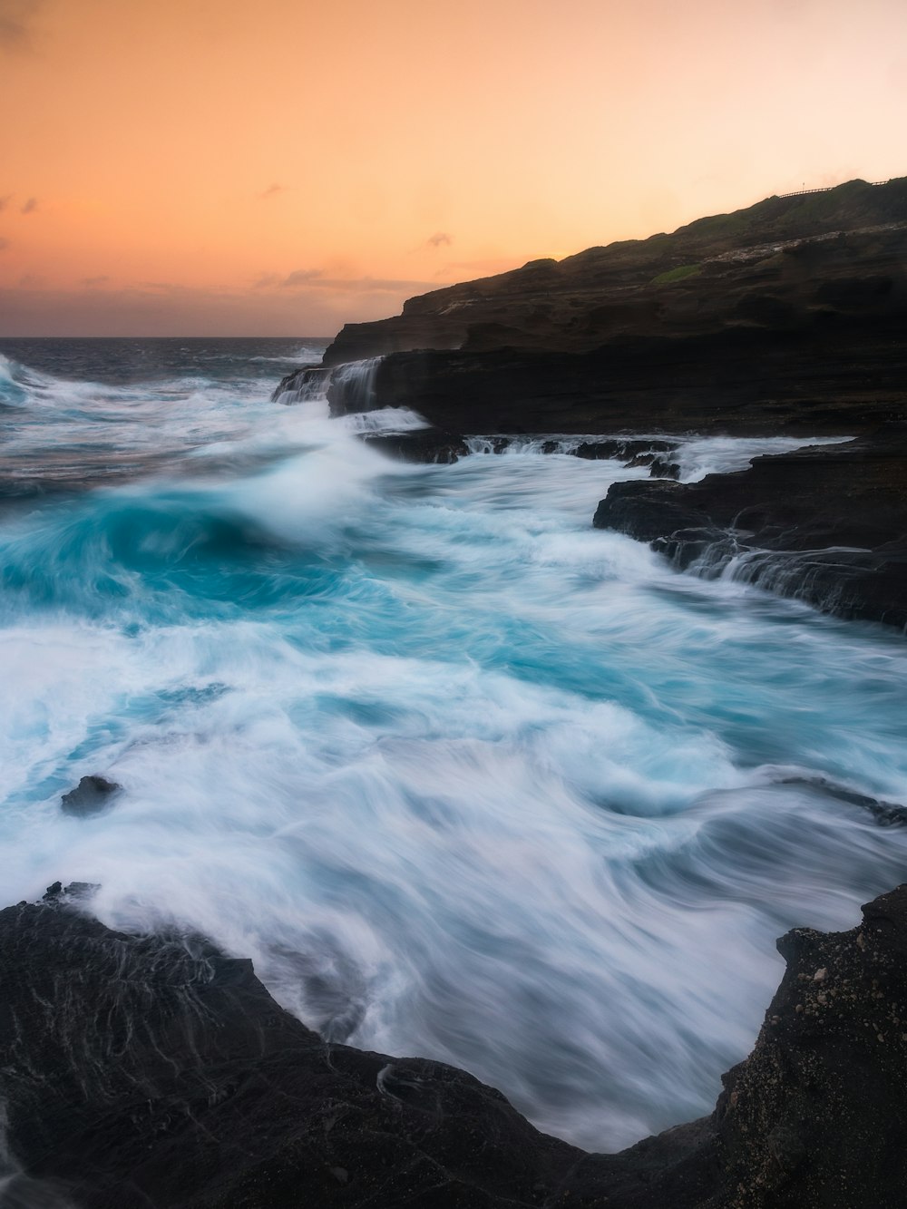 ocean waves crashing on rock formation during sunset