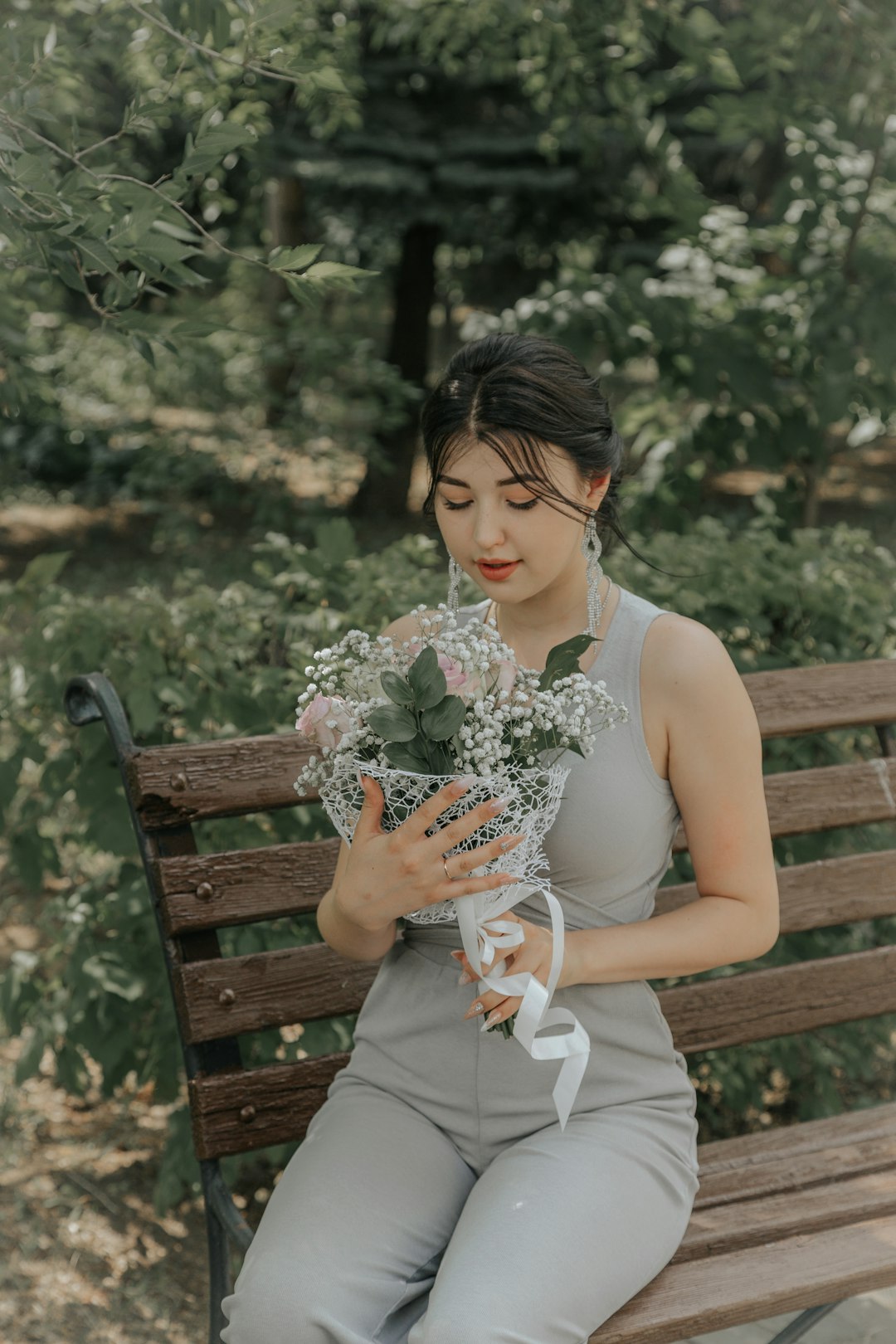 woman in white sleeveless dress sitting on brown wooden bench holding bouquet of flowers