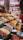 An organized display of various colorful spices and herbs in a vibrant marketplace. The spices are neatly arranged in rows, each with a distinctive color and texture, creating a visually appealing pattern. A large banner with 'Hazer Baba' is visible in the background, emphasizing a focus on quality.
